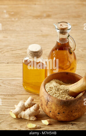 Bellissima cucina vita ancora due vetro trasparente olio vasi, mortaio di legno pieno di macinare spezie e pestello con radice di zenzero su tavola in legno rustico, c Foto Stock