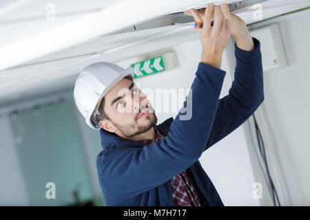 Elettricista maschio con un cacciavite la riparazione sensore fuoco Foto Stock