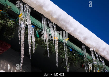 Neve e ghiaccio con luci natalizie e ghiaccio appesi le grondaie su un edificio in inverno Foto Stock