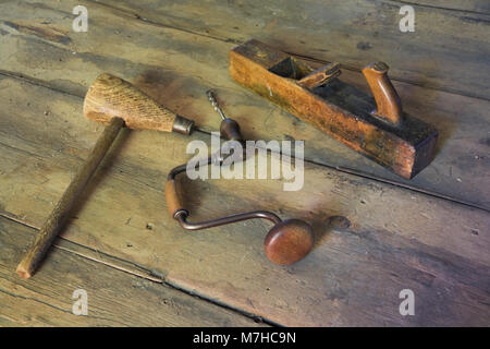 Vecchia mallet, manuale trapano a mano e piano a mano sul pavimento in legno nella camera a vuoto all'interno di un vecchio 1800s cottage in stile casa. Foto Stock