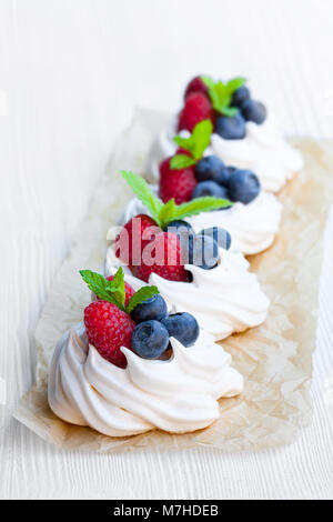 Mini Pavlova meringa torte con bacche e foglie di menta bianca su sfondo di legno Foto Stock