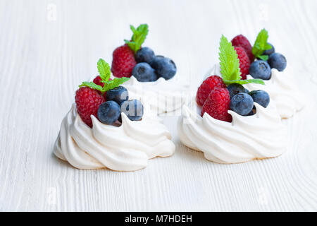 Mini Pavlova meringa torte con bacche e foglie di menta bianca su sfondo di legno Foto Stock