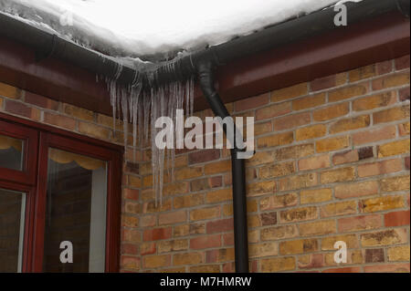 Leggero riscaldamento del tetto della casa e la neve di fusione causando accumuli icicle congelati grondaie e il possibile ingresso di acqua nelle pareti Foto Stock
