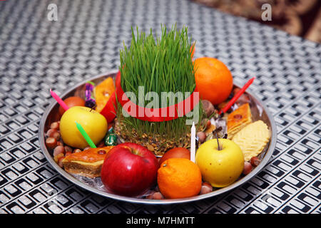 Novruz la piastra del vassoio con l'Azerbaigian nazionale pakhlava pasticceria e shecurbura viola foulard di seta . Semeni sulla piastra vintage decorata con cordoncino rosso in stile nazionale tovaglia . Apple, candela, i dadi . Foto Stock