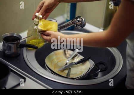 Il lavaggio delle stoviglie. mani in schiuma lava la padella con un detergente e una spugna nella cucina della casa Foto Stock