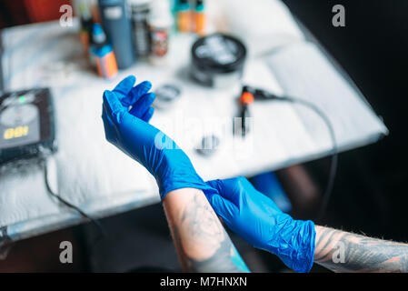 Femmina artista tattoo mani in blu guanti sterili, professional strumenti di lavoro in background. Tatuaggio in salone Foto Stock