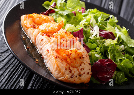 Cibo delizioso: salmone al forno con gamberi in salsa di miele e insalata fresca su una piastra di close-up su una tavola orizzontale. Foto Stock