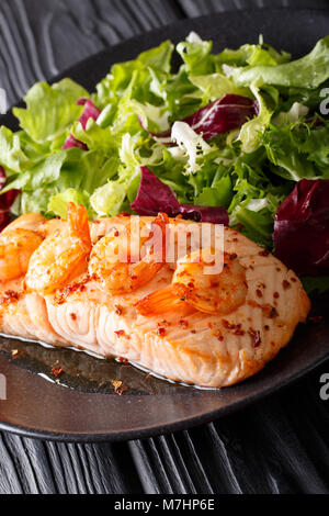 Di salmone al forno con gamberi e salsa di miele con un contorno di insalata mix di close-up su una piastra su un piano verticale. Foto Stock