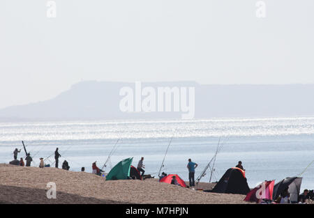 I pescatori in un Haze di calore su un bruciante giorno su Chesil Beach UK, alcuni ledgering, altri pesca dello sgombro. L'isola di Portland in background. Foto Stock