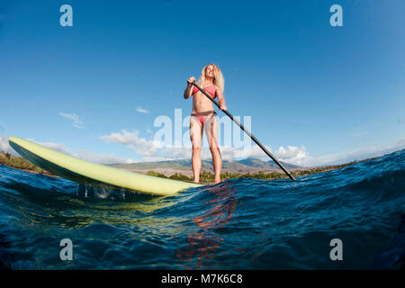 Istruttori di Surf Tara Angioletti su uno stand up paddle board off Bearch canoa, Maui. Hawaii. Le montagne di West Maui sono in background. Immagine è mo Foto Stock