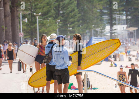 Donna che trasportano le tavole da surf a parlare con un bagnino a Manly Beach a Sydney, Australia Foto Stock