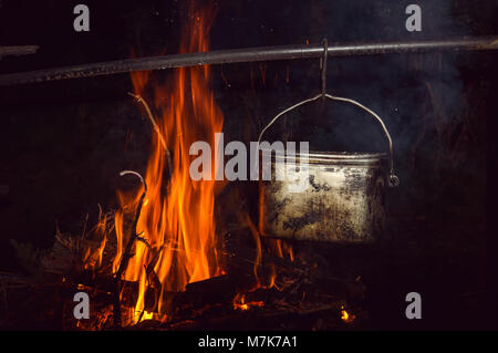 Acqua bollente in bowler nel falò. Escursionismo romanticismo intorno al fuoco di notte. Foto Stock