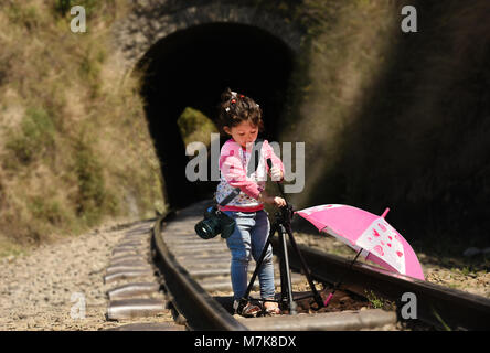 Bambina fotografo con treppiede e fotocamera DSLR strapped sulla sua spalla. Foto Stock