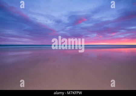 Una bella rosa e blu tramonto riflesso nella sabbia bagnata su una spiaggia in Westfjords, Islanda. Foto Stock