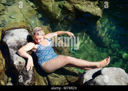 Una giovane donna rilassante sulle rocce a tre piscine nuoto foro in Oregon. Foto Stock