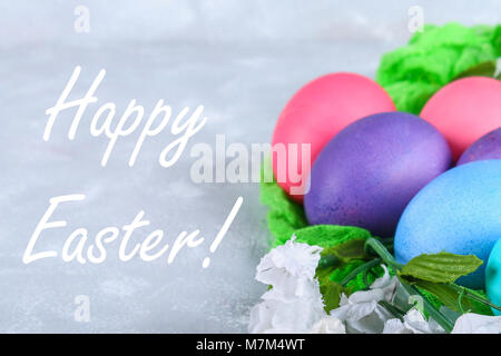 Colorate le uova di pasqua con fiori di colore bianco su un cemento grigio sfondo Foto Stock