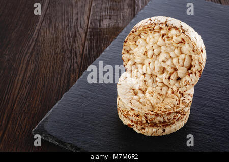 La dieta torte di riso pila sul pezzo scuro del bordo si stabilirono su vintage tavolo in legno rivestito con homespun igienico, il fuoco selettivo di close-up. Alcuni di questi testi spa Foto Stock