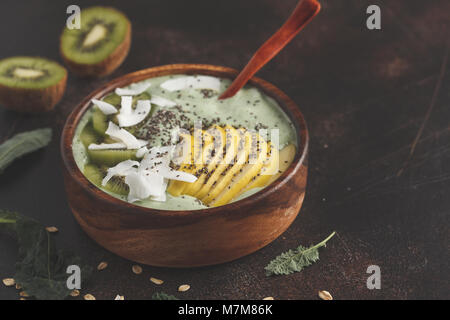 Cavolo verde frullato vegano ciotola con noce di cocco, chia, mela e kiwi. Sano cibo vegan concetto. Scuro dello sfondo arrugginito, vista dall'alto Foto Stock