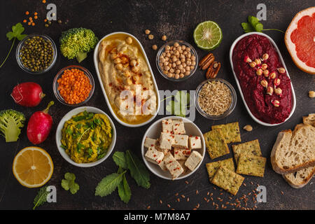 Cibo Vegan sfondo. Spuntini vegetariani: hummus, barbabietole hummus, piselli verdi dip, verdure, tofu. Vista superiore, sfondo scuro, copia dello spazio. Foto Stock