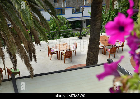 Wooden garden furniture on a terrace seen through lush plants, high angle shot Foto Stock