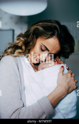 Mamma orgogliosa che porta il suo figlio in una imbracatura e guardando verso il basso verso di lui mentre dorme tranquillamente Foto Stock