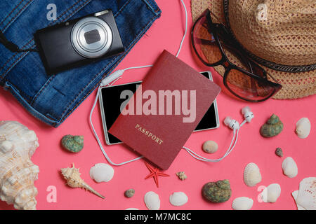 Passaporto, Smartphone, vestiti, occhiali da sole, Fotocamera, marrone cappello, su sfondo rosa. Vista dall'alto concetto di viaggio. Foto Stock