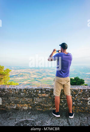 Uomo di scattare le foto di Trapani scenario sul suo telefono cellulare in Erice, in Sicilia Isola, Italia Foto Stock
