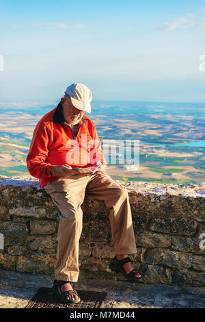 Erice, Italia - 18 Settembre 2017: Senior uomo lettura mappa turistica di Erice, in Sicilia Isola, Italia. Scenario di Trapani sullo sfondo Foto Stock