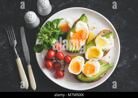 Uovo affogato e avocado toast sulla piastra bianca, vista dall'alto, tonica immagine. Una sana prima colazione o il pranzo Foto Stock