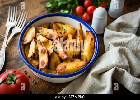 Spicchi di patate o di patate al forno guarnite con prezzemolo sul vecchio tavolo rustico. Messa a fuoco selettiva Foto Stock