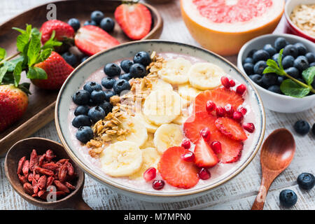 Ciotola smoothie alla fragola, banana, mirtillo, melograno e scaglie di noce di cocco, primo piano. Concetto di stile di vita sano, mangiare sano, vegan, v Foto Stock