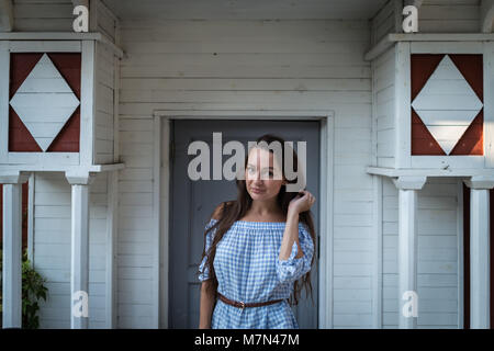 Giovane donna si trova all'ingresso di uno stile Coloniale in legno casa bianca. Bella ragazza sullo sfondo del vecchio edificio elegante con arredamento Foto Stock