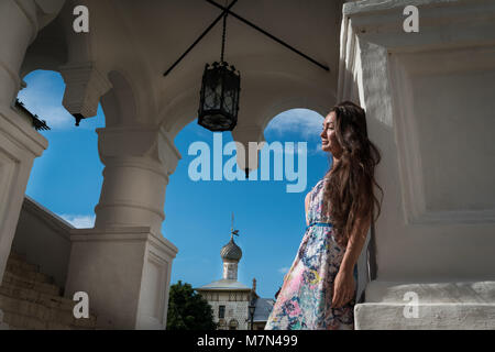 Bella giovane donna in abito leggero si trova all'ingresso della chiesa sullo sfondo del cielo blu e nuvole Foto Stock