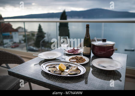 Bella tabella con il cibo locale e vino sul balcone della casa. Concentrarsi sulle ostriche. Sullo sfondo di un mare e monti. Still Life Foto Stock