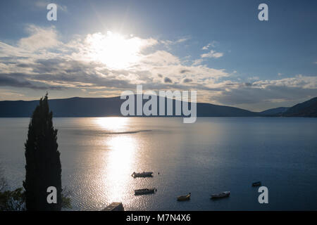 Tramonto con nuvole drammatico sullo sfondo della baia e delle montagne. Bella riflessione sull'acqua. Nuvole e cielo in Montenegro. Piccole imbarcazioni vicino al molo Foto Stock