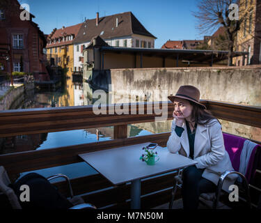 Giovani pensieroso donna si siede a tavola in caffetteria sulla terrazza e guardare il paesaggio urbano e il lungomare in piccole città europea Foto Stock