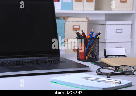 Close-up di comodo posto di lavoro in un ufficio con computer portatile, un mouse, notebook, bicchieri, penna e altre apparecchiature posa sulla tavola su blur backg mobili Foto Stock