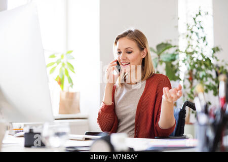 Imprenditrice in sedia a rotelle alla scrivania nel suo ufficio. Foto Stock