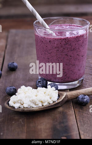 Il Kefir grani in cucchiaio di legno nella parte anteriore del mirtillo Kefir frullato. Il Kefir è uno dei top salute alimenti disponibili fornendo potenti probiotici. Foto Stock