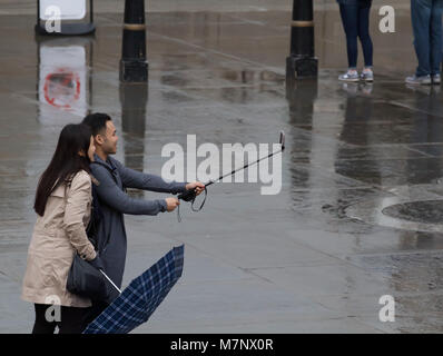 Piccadilly Circus, Londra, Regno Unito. Xii Mar, 2018. Un paio di scattare una foto utilizzando una bacchetta selfie su un opaco, umido e triste giorno a Londra. Acquazzoni pesanti sono attesi nel corso di tutta la settimana attraverso la maggior parte del paese, con il Met Office di avvertimento turbate condizioni e perfino la possibilità di temporali Credito: Keith Larby/Alamy Live News Foto Stock