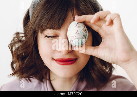 Bella ragazza elegante nelle orecchie di coniglietto holding uovo di pasqua presso gli occhi e relax su sfondo bianco con spazio per il testo. divertente caccia di pasqua concetto. felice Foto Stock