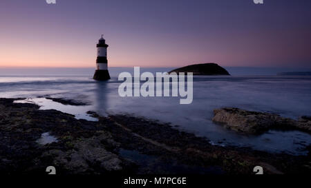 Penmon Point lighthouse e isola dei puffini, Anglesey, Galles del Nord Litorale con alghe marine rocce coperte al crepuscolo Foto Stock