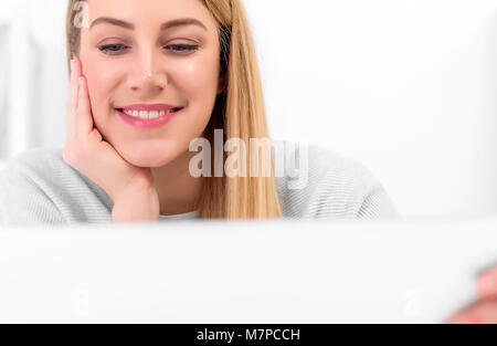 Giovane donna sta lavorando a un computer notebook o tablet pc in un buon umore. La bionda alla sua scrivania a casa o in ufficio con un computer portatile e un bicchiere di rosso. Foto Stock