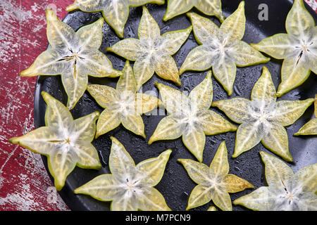 Gustosi pezzi di fettine di carambola sul bagnato la piastra nera sul malandato in legno tabella rossa. Primo piano top view photo. Orizzontale. Foto Stock