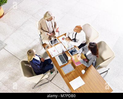 Quattro multi-etnico business aziendale persone che si incontrano in un ufficio moderno edificio, ad alto angolo di visione. Foto Stock