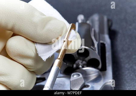 Snubnose revolver con cilindro aperto in preparazione per essere pulita con una mano inserendo un patch di cotone nella pistola asta di pulizia isolato sul tappetino nero Foto Stock