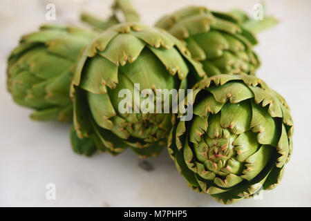 Quattro di carciofi crudi su una tavola di marmo closeup. Il fuoco selettivo sulla parte anteriore bud Foto Stock