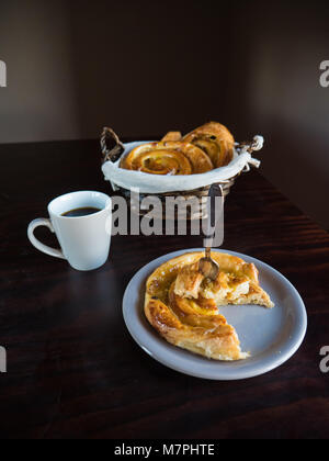 Vista verticale del francese raisin pasticceria su una piastra bianca e cesto di vimini con una tazza di caffè su di un tavolo di legno Foto Stock