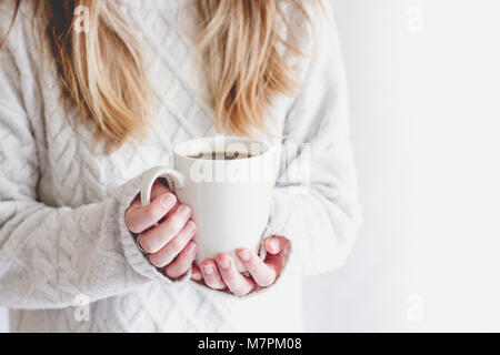 Una sezione mediana di una bionda ragazza dai capelli con in mano una coppa di bianco isolato su un fondo bianco in un accogliente stile di vita dell'immagine. Foto Stock