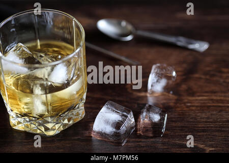 Whisky in un bicchiere e pezzi di ghiaccio su un legno Foto Stock